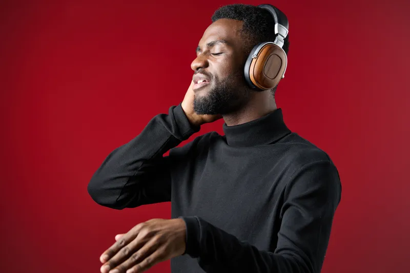 A young Black man enjoying music with headphones on a red background, expressing joy and relaxation, perfect for promoting music enjoyment and culture