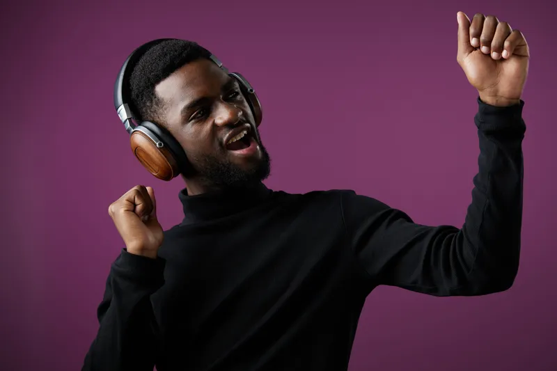 Happy young man dancing with headphones on a purple background, celebrating music and joy in a stylish outfit Music, happiness, dance, headphones, emotions, joy, black man