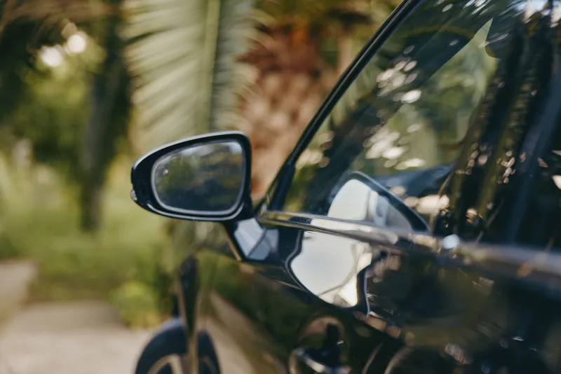 car side mirror reflection black car vehicle tropical closeup of glossy door and mirror with palm tree bokeh in background, automotive exterior detail and luxury finish