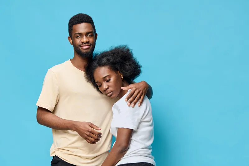 Young African couple sharing a tender moment against a bright blue background, showcasing love, connection, and warmth in casual clothing