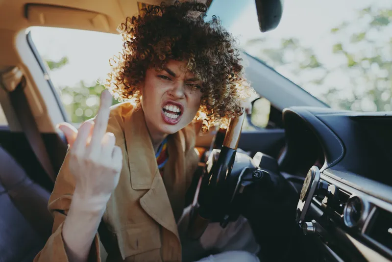 Young woman in a car shows defiant attitude in a sunlit moment, leaning forward with a bold expression and arched back, capturing rebellious energy and urban edge