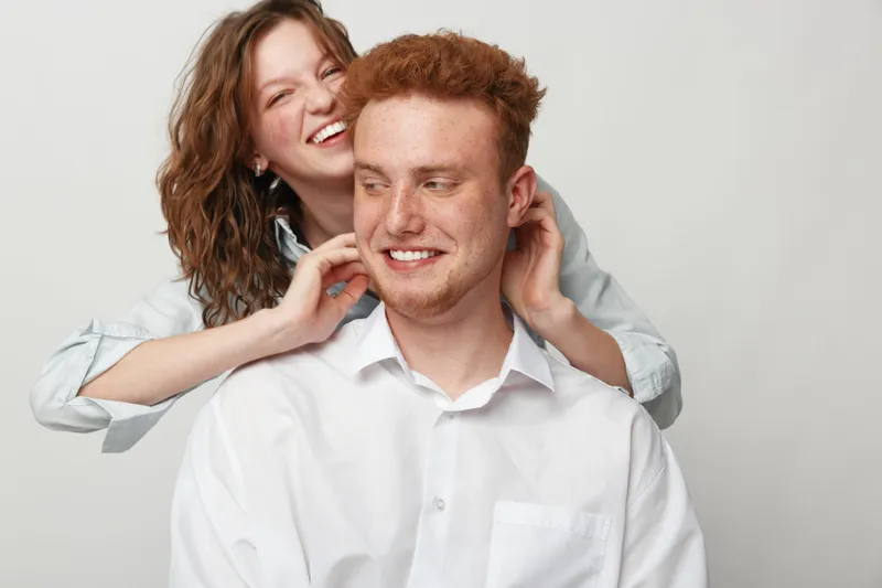 Happy young couple in white shirts smiling and enjoying playful moment together on light background. Concept of love, friendship, relationship, and positive emotions.