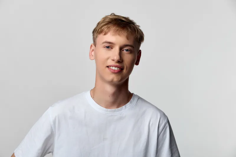 Young man in a white t shirt smiles softly in a bright studio with a neutral background, conveying casual confidence, approachable mood, and everyday style for stock use in lifestyle campaigns