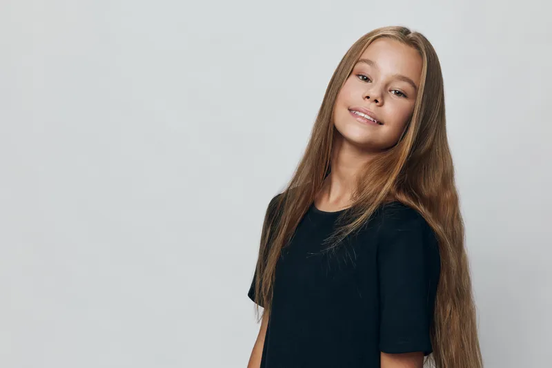 Girl with long straight hair smiling and posing in front of grey background casual t shirt portrait, happy expression and natural beauty in studio photo session.
