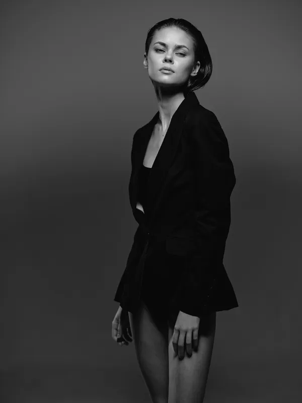 black and white portrait of a confident woman wearing a dark blazer posing against gray background