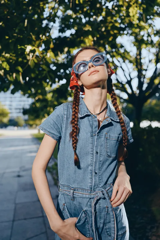 Modern boho-western denim street style woman wearing sunglasses and a red bandana confidently enjoying sunny outdoor urban lifestyle with film color tones.