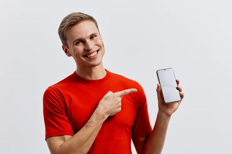 smiling man in red t-shirt pointing at phone screen holding mobile device white background digital detox concept technology connection
