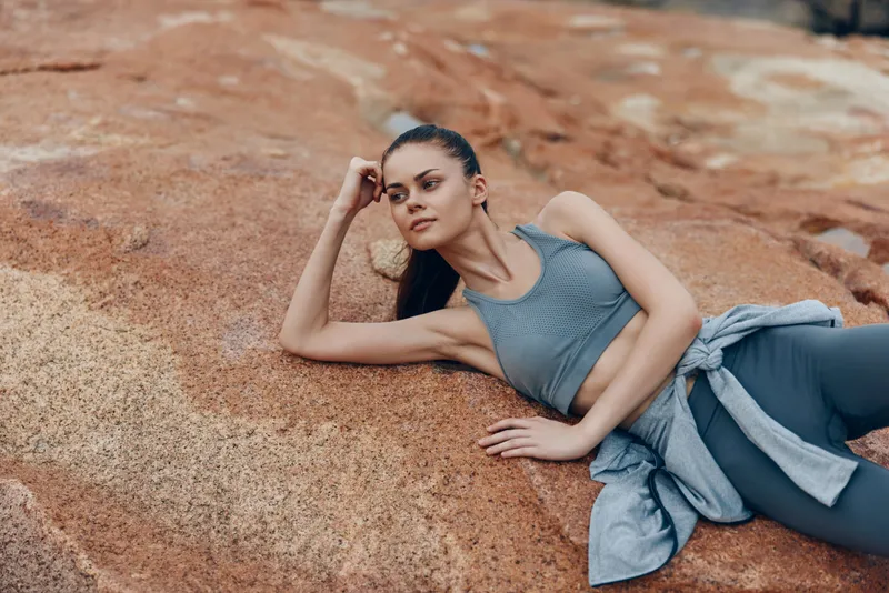 Young athletic woman in stylish sportswear relaxing on rocky terrain, embodying health and fitness lifestyle, with focus on nature and active leisure