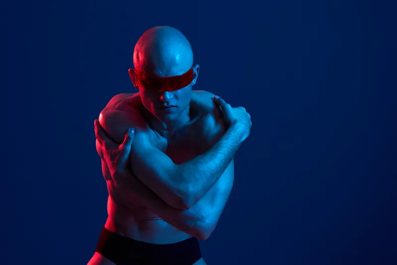 A dynamic man poses dramatically in blue and red light, showcasing strength and emotion. The black and white tones emphasize the artistry of the scene.