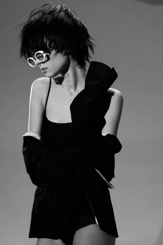 Black and white portrait of stylish woman wearing sunglasses and fashionable outfit with dramatic mood and edgy hairstyle.