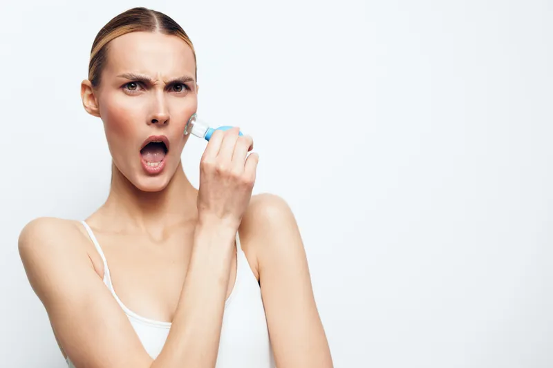 Woman using inhaler spray indoors on a white background, mouth open breathing medicine, focused expression, health concept, modern wellness mood, soft light, minimal composition