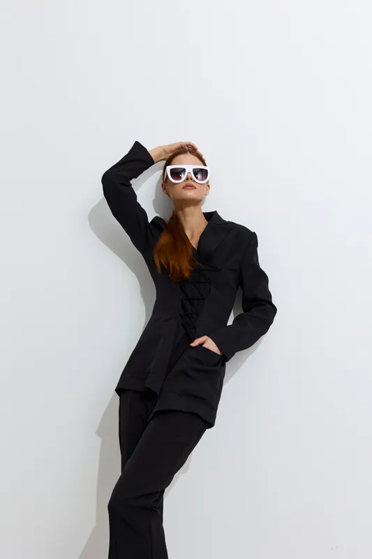 Fashion woman in stylish black outfit and white sunglasses posing confidently against white background, showcasing modern beauty and high-fashion elegance.