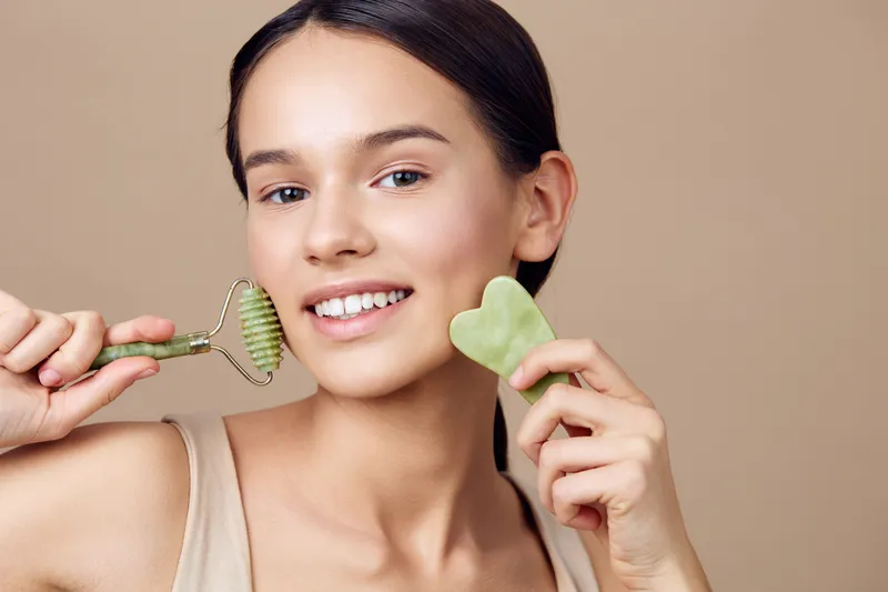 Young woman smiling with a facial roller and heart shaped jade stone, promoting skincare and self care concepts for glowing skin