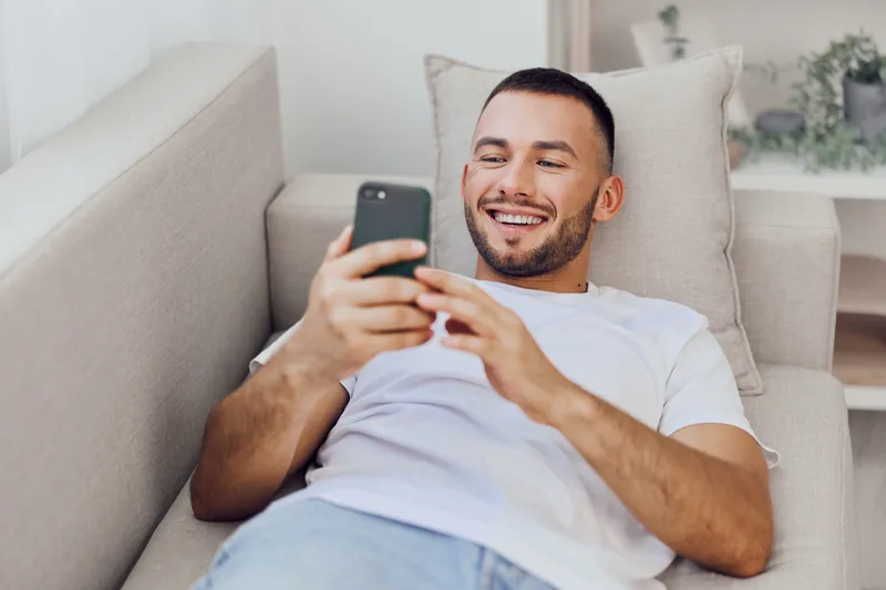 Relaxed man enjoying a digital detox while scrolling through his phone, reflecting on the balance between technology and mental health in a cozy home setting.