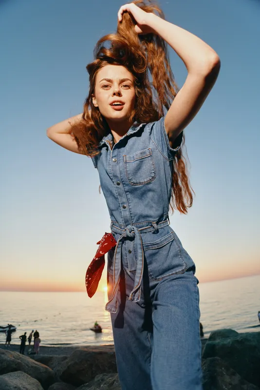 Lifestyle woman in modern boho-western denim street style with long hair, playful pose, and film color effect capturing natural sunset ambiance.