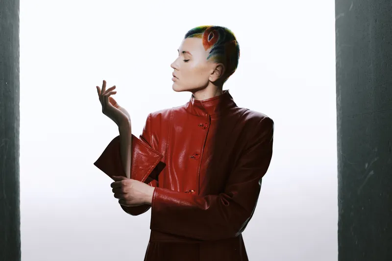 woman with colorful hair and avant-garde style wearing red leather jacket, artistic pose against bright background, modern and edgy fashion.