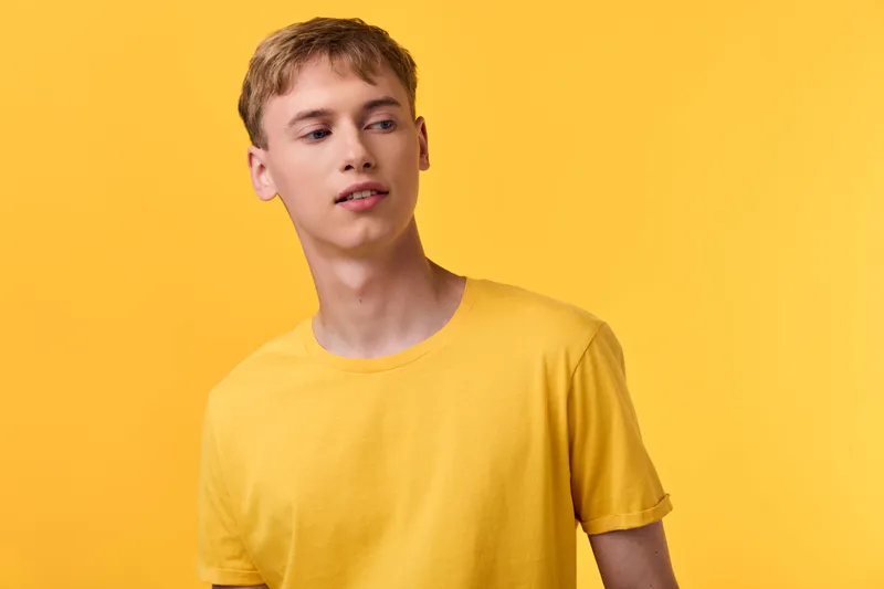 Yellow clad man in tshirt poses casually against a bright studio yellow background, showcasing minimalist fashion, warm lighting, modern style and clean composition for lifestyle, color harmony and