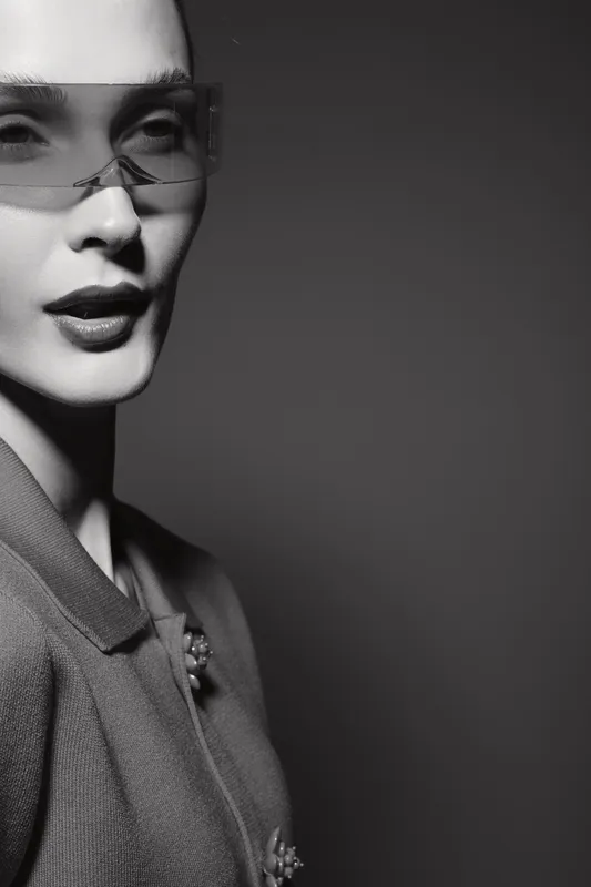 Black woman with dark skin wearing sunglasses and a stylish jacket in black and white portrait with dramatic lighting.