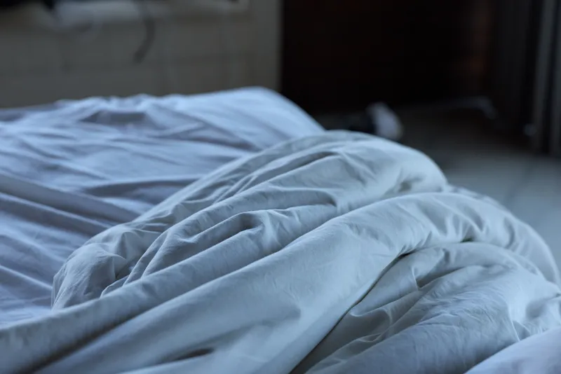 Unmade bed with wrinkled white sheets captures a quiet morning moment in a softly lit bedroom with a cozy and relaxed atmosphere.