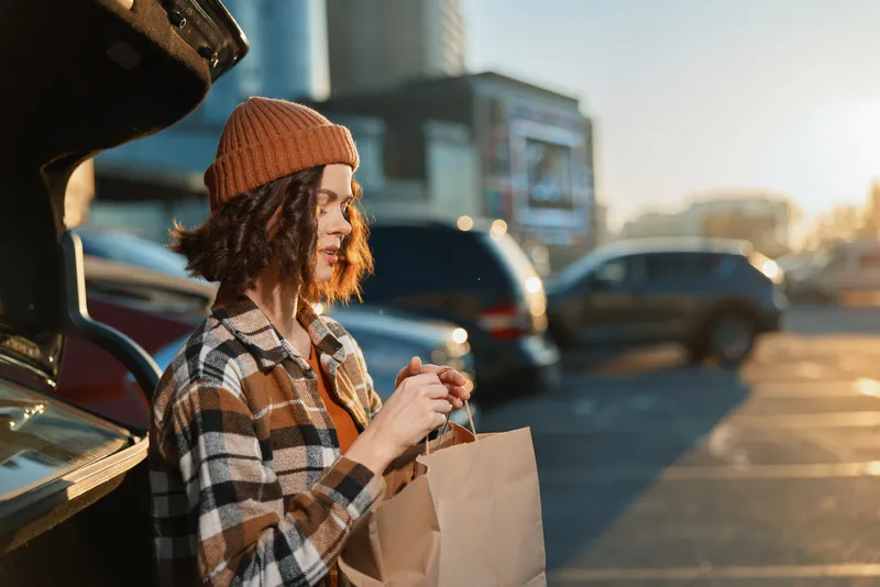 Woman bag parking car beanie sunlight candid authenticity in urban portrait. Golden hour glow, candid lifestyle scene with mindful living and emotional storytelling mood and warm backlight.