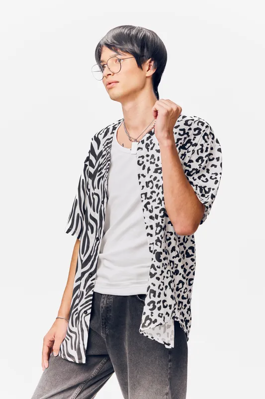 young man wearing stylish animal print shirt and glasses poses confidently against white background, casual fashion look with relaxed mood