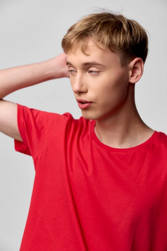Confident young man in a red shirt poses with hand at back of head, casual style, thoughtful gaze, studio lighting, clean background, fashion mood, easy to use for diverse projects
