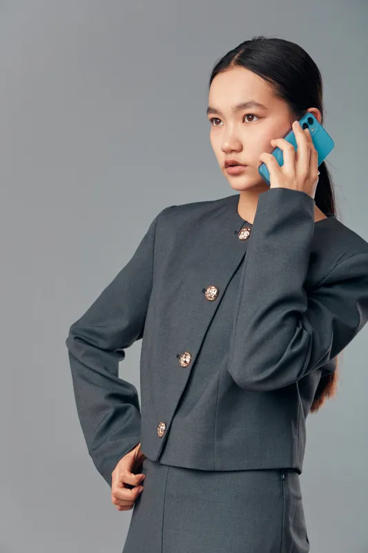 Young woman in gray business suit talking on smartphone with serious expression against neutral background. Professional communication, technology and mobile phone concept in studio portrait.