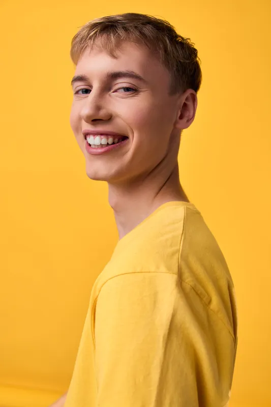 Smiling young man in a yellow shirt against a bright studio backdrop, casual pose conveys happiness, warmth and confidence for lifestyle or fashion use