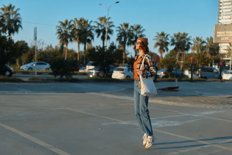 woman jump parking palm sunglasses tote urban coast scene at golden hour, candid lifestyle portrait with authenticity, golden hour glow and emotional storytelling capturing joyful motion