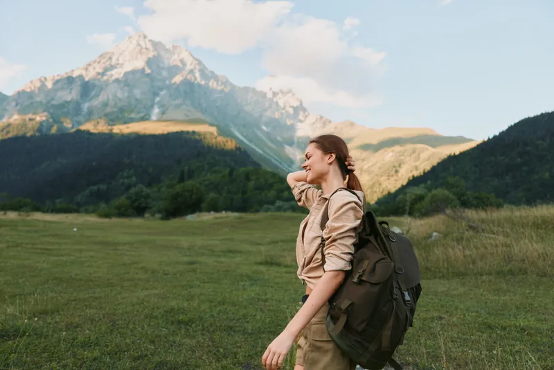 Bright woman outdoors hiking backpack nature mountain scenery travel leisure, enjoying sunny day with relaxed posture and meadow backdrop
