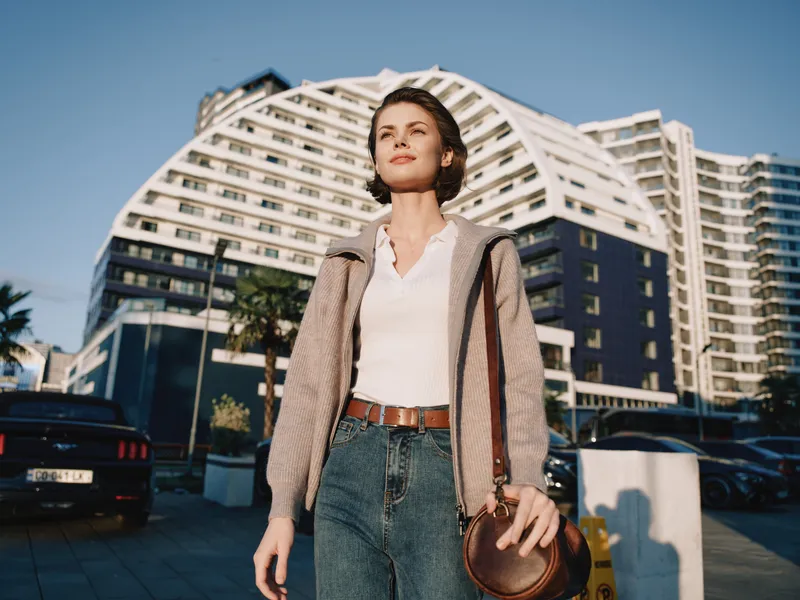 A confident professional woman walks through a sleek urban scene. She wears smart casual attire and carries a warm expression, projecting purpose, focus, and modern momentum in a dynamic city setting.