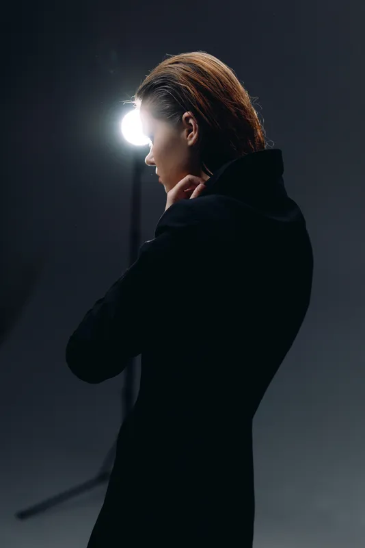 Profile of a thoughtful woman in black coat with bright light background in dark studio setting