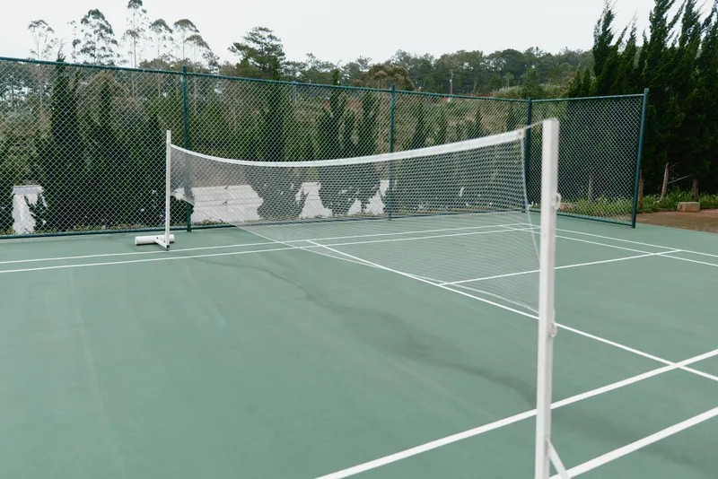 Professional tennis court with a clear green surface, surrounded by lush greenery, perfect for sports photography and athletic concepts