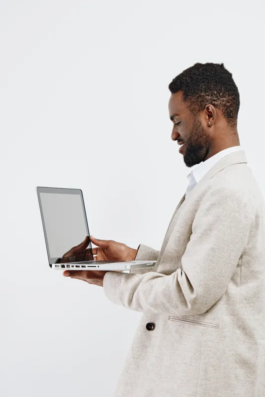 Confident man in beige suit holding laptop and looking at screen, isolated on plain white background, studio portrait, professional style, business concept, technology, modern, successful