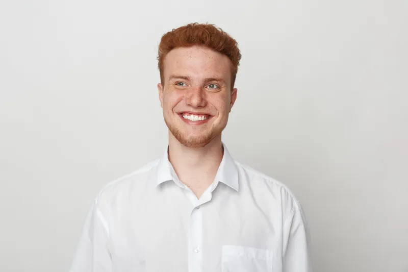 Smiling young man with red hair and beard wearing white shirt looks away with happy expression. Studio portrait on light background. Concept of positivity, youth, and casual style.