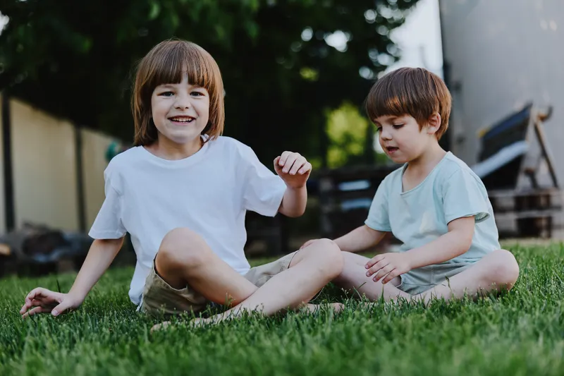 Joyful boys playing together on a sunny day, enjoying their childhood in the grassy garden. The smile on one boy's face captures the essence of happiness and freedom. ###