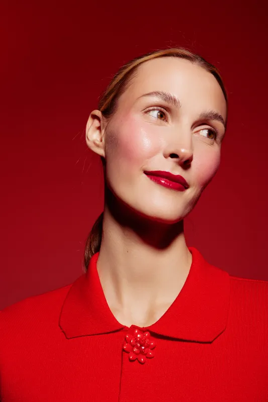 Portrait of a smiling woman with red lipstick and red clothing on red background. Concept of beauty, fashion, elegance, and confident female model with smooth skin and natural makeup.