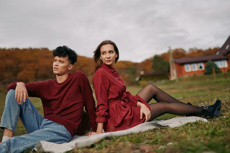 Young couple sits on a blanket in a rural autumn field, sharing a genuine relaxed pose and eye contact that convey authenticity and credibility, captured in natural light and a candid moment.