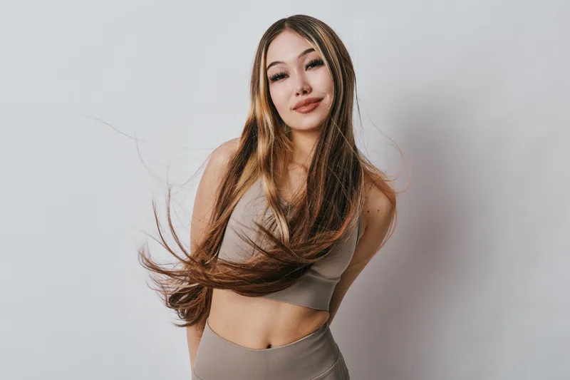 Young woman with long flowing hair posing in sleeveless crop top and skirt against gray studio background for fashion beauty portrait and hair care concept.