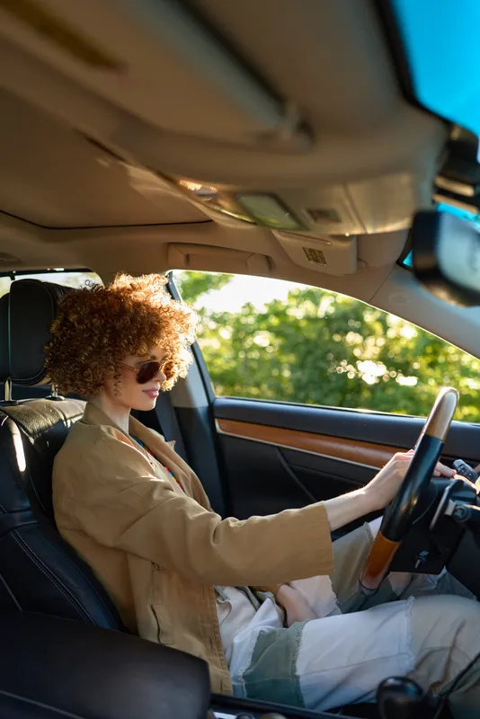 Woman driving car interior with sunglasses, curly hair, fashion lifestyle retro mood, warm daylight tones, cinematic look, relaxed confident pose, daylight reflections on dashboard, vintage vibe,