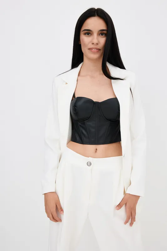 woman wearing white suit and black leather corset top stands confidently against plain white background, showing modern fashion style and minimalist elegance