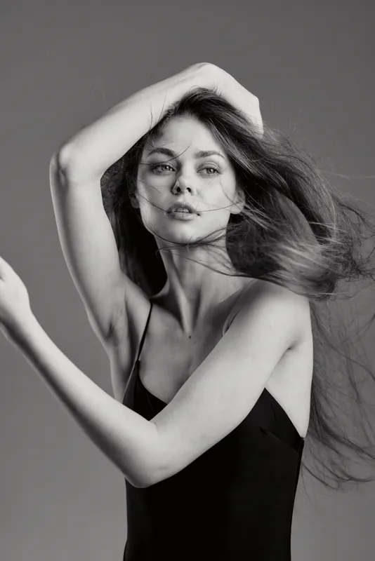 Black and white portrait of a young woman with flowing hair in a minimalist dress, expressing elegance and natural beauty.