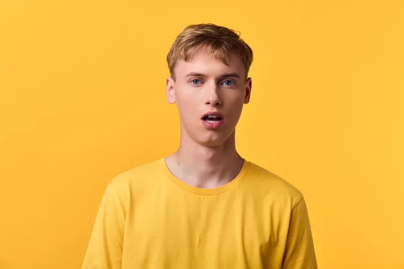 Closeup of a young man in a yellow shirt against a bright yellow backdrop, casual studio shot highlighting expression, mood, and style in a clean composition