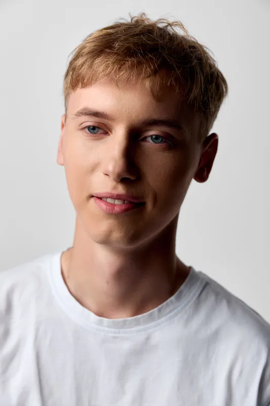 Young man in a white shirt with a soft smile, studio lighting, and relaxed pose, suitable for lifestyle, fashion, and wellness topics in editorial and commercial projects