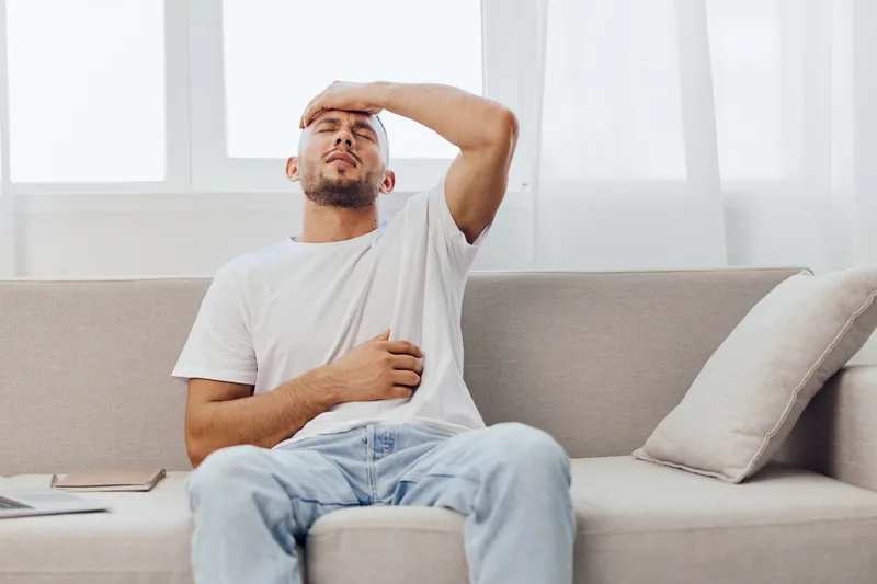 Frustrated man holding his forehead while sitting on a cozy sofa, expressing stress and fatigue. This scene captures the essence of modern life's challenges.