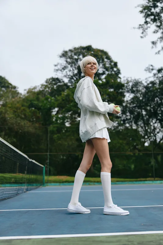 Young woman with short blonde hair in sporty outfit enjoying tennis on the court, showcasing fitness, joy, and an active lifestyle amid lush greenery