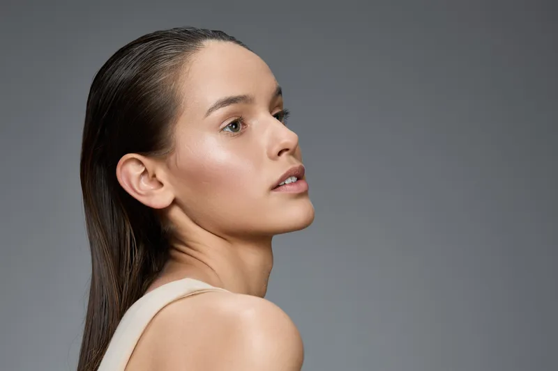 Portrait of a young woman with long hair, showcasing natural beauty and healthy skin against a grey background, conveying elegance and serenity
