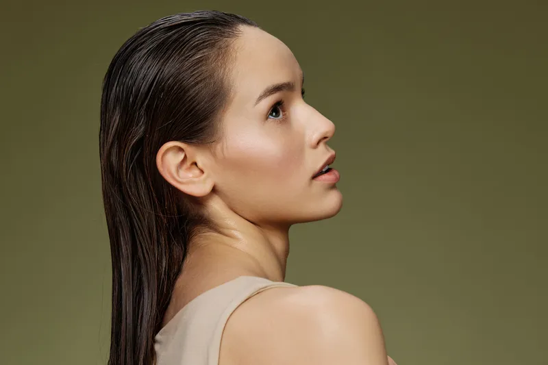 Elegant profile portrait of a young woman with wet hair, showcasing natural beauty and calm emotions against a muted green background