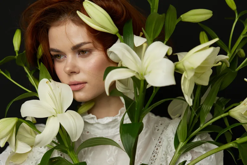 Portrait of a young woman with red hair surrounded by white lilies, expressing serenity and beauty in a soft, elegant atmosphere