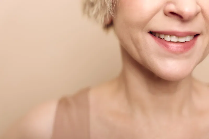 Closeup of smiling mature woman with natural skin texture and light makeup on beige background. Concept of aging gracefully, beauty, confidence, and healthy skin care routine.